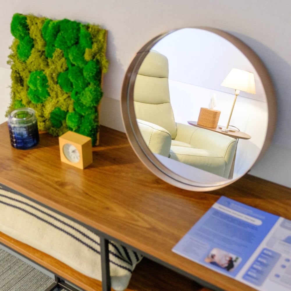 Moss art sitting on a table next to a mirror reflecting a white chair
