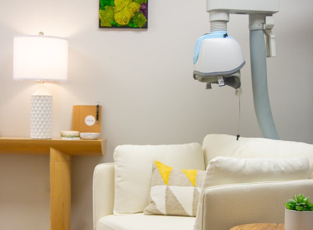 Brainsway TMS machine helment over a comfy white chair against a white wall with moss art handing and a lamp on a side table