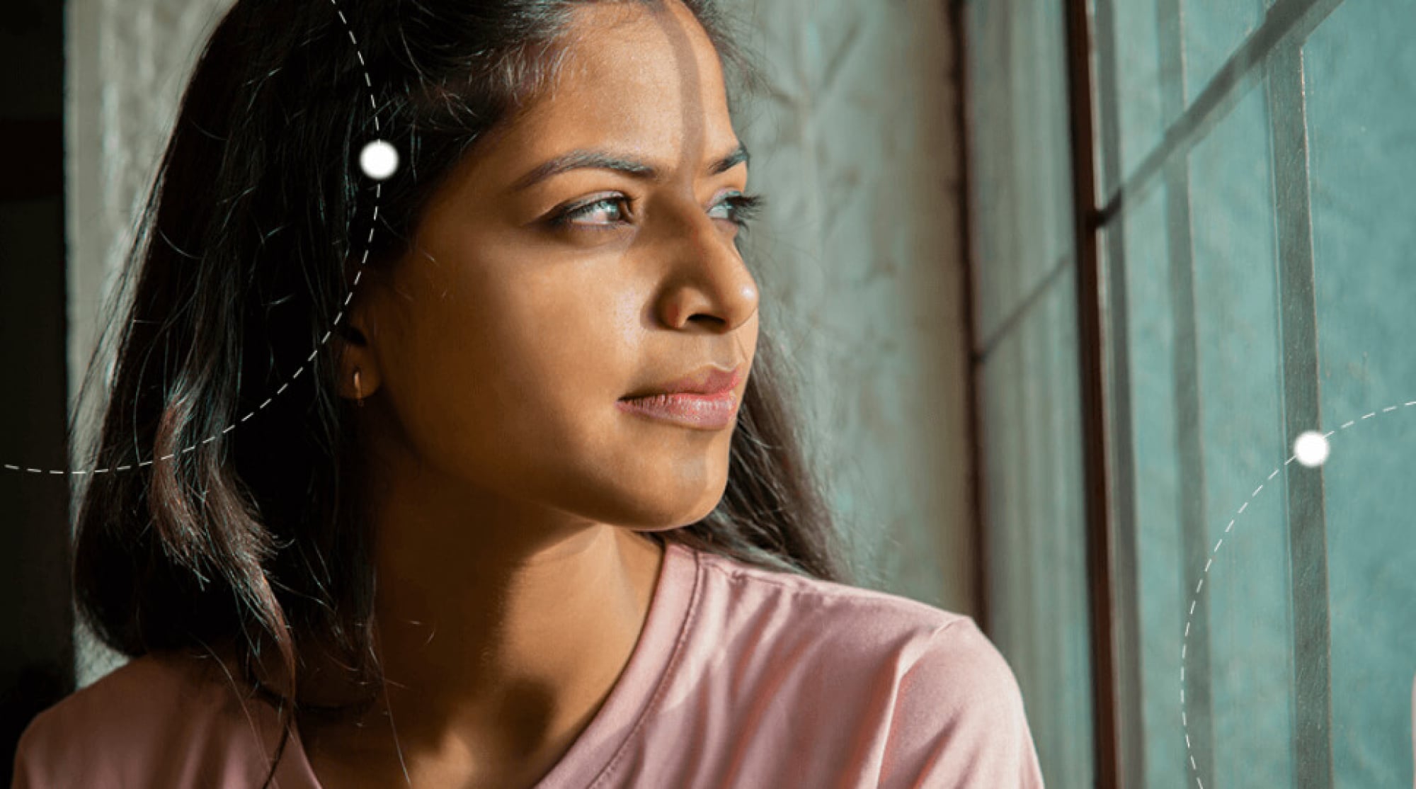 A young woman in a pink top looks out a window